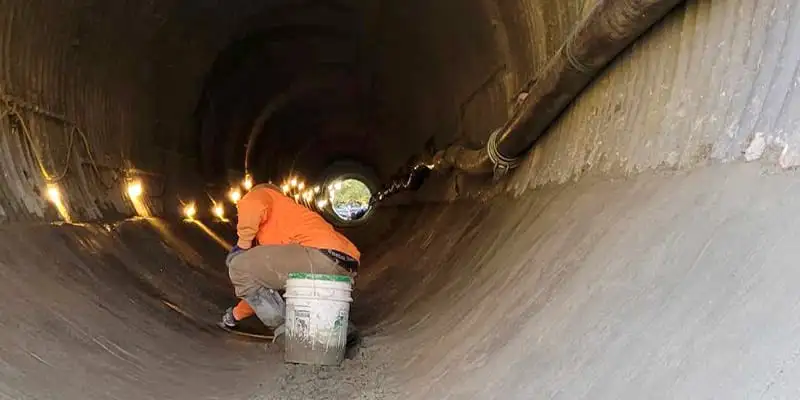 A technician smoothing out concrete that has been used to coat the invert of this culvert