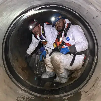 Two Technicians Sitting Inside A Pipe Near A Joint Sealed With HydraTite