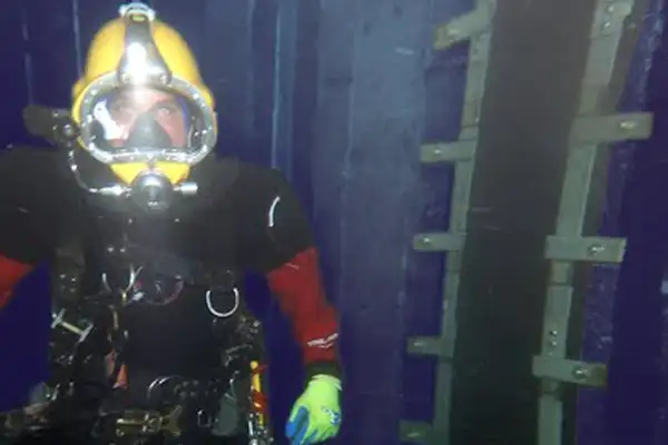 A diver kneeling near a joint sealed with HydraTite in a submerged pipe
