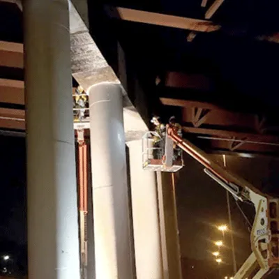 Carbon fiber fabric being applied by a technician in a lift to strengthen a bridge's supports