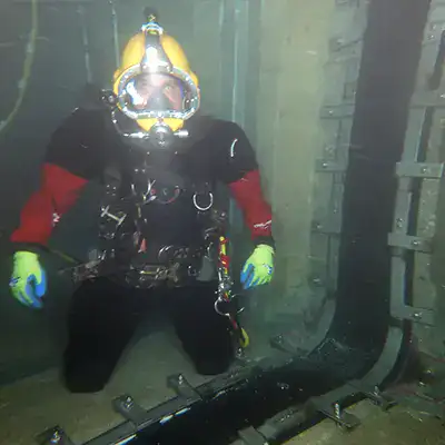 A diver kneeling near a joint sealed with HydraTite in a submerged pipe