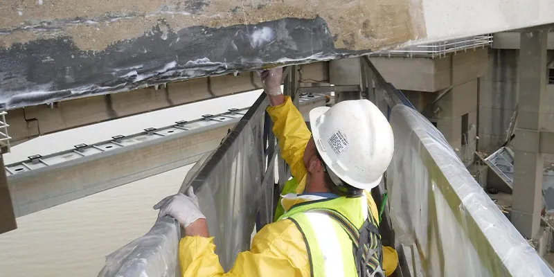 A technician applying epoxy to the underside of a bridge
