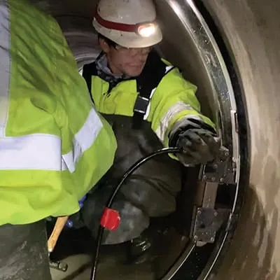 Two technicians sitting in a pipe, installing HydraTite over a joint