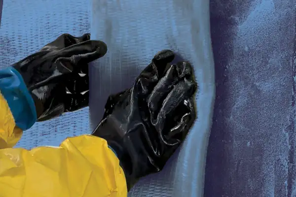 A pair of gloved hands positioning a portion of saturated fiber fabric onto a concrete structure