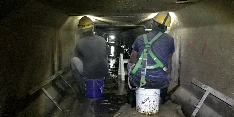 Two employees inside a pipe sitting on buckets as they prepare to install HydraTite seals over a joint in this irregularly-shaped pipe