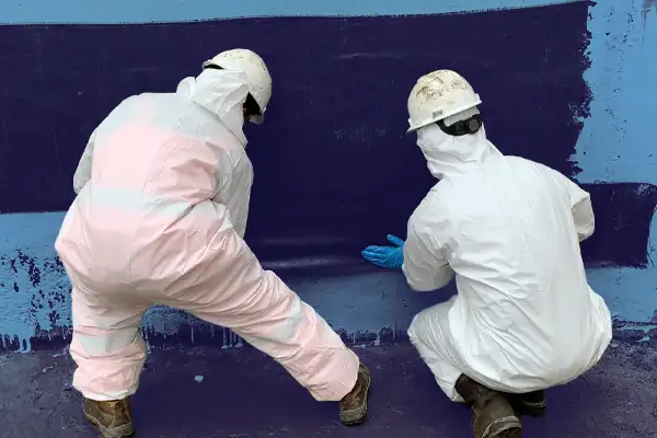 Two technicians in tyvek applying saturated carbon fiber fabric to a concrete wall that has been coated in primer epoxy